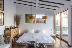 A modern bedroom with a large bed, wooden flooring, a wooden cabinet, and a view through a large window.