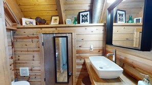 A wooden cabin bathroom with a white sink, a mirror, and a door leading to a shower area.