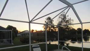A covered outdoor area with a pool, lounge chairs, and a view of a lake and surrounding buildings during sunset.