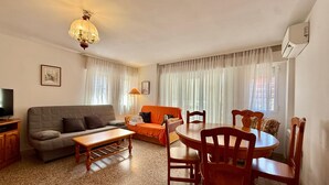 Un soggiorno con un divano, un tavolo, sedie, una televisione e un lampadario.