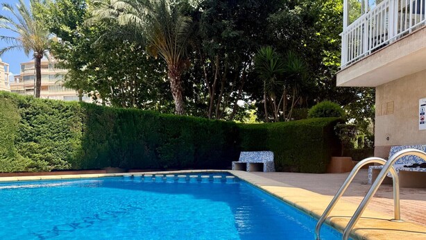 Una piscina con una scala metallica, circondata da vegetazione e un edificio con un balcone.