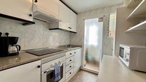 Una cucina moderna con mobili bianchi, una macchina da caffè nera, un forno a microonde e una finestra con persiane.