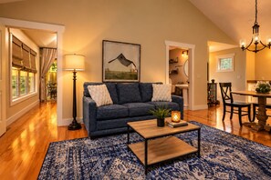 A living room with a blue sofa, a coffee table, a patterned rug, and a painting on the wall. - Private Hot Tub, Quiet Setting, Spotlessly Clean Cottage (Asheville)