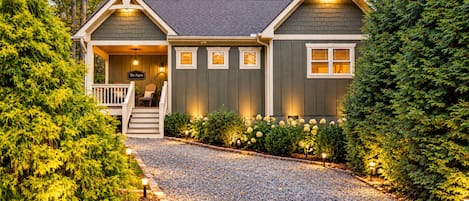 A two-story house with a front porch, a staircase, and a gravel driveway.