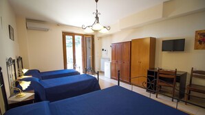 Quarto de hotel com três camas, um guarda-roupa de madeira, uma televisão e um radiador.