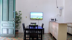 Un coin repas avec une table et des chaises, un téléviseur fixé au mur, un four à micro-ondes posé sur le comptoir et une plante en pot.