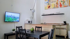 A dining area with a table, chairs, a television, a microwave, and kitchen shelves. - Gladioli 1101 - That's all Puerto Rico (Ponce Pueblo)