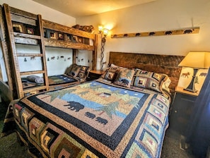 Quarto com duas beliches, uma cama grande com colcha estampada e decoração de animais nas paredes.