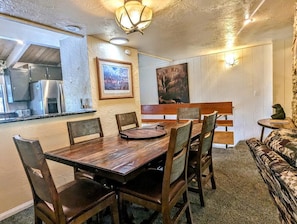 Uma área de refeições com uma mesa e cadeiras de madeira, um banco e uma pequena mesa com uma estátua.