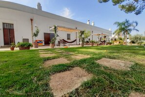 A white building with a covered patio area, potted plants, and a hammock.