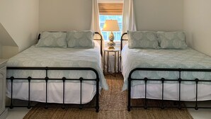Une chambre avec deux lits jumeaux, une petite table ronde avec une lampe et une fenêtre avec des rideaux.
