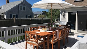 Une terrasse en bois avec une table et des chaises, un barbecue et un espace abrité avec un parasol.