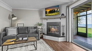 A modern living room with a fireplace, a sofa, a coffee table, and a large window offering a view of the outdoors. - Izaty's Beach Villa- Completely remodeled and exceptionally clean (Onamia)