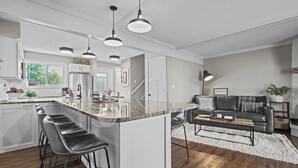 A modern kitchen with a central island, bar stools, pendant lighting, and a view of the living area with a sofa and coffee table. - Izaty's Beach Villa- Completely remodeled and exceptionally clean (Onamia)