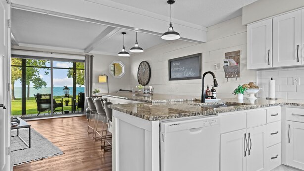 A modern kitchen with white cabinets, granite countertops, and a large island. There is a dining area with chairs and a table, and a view of the outdoors through large sliding doors. - Izaty's Beach Villa- Completely remodeled and exceptionally clean (Onamia)