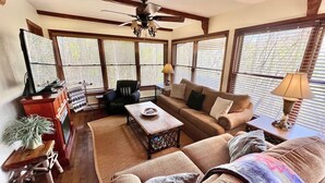 A cozy living room with a sofa, armchair, and coffee table, large windows with blinds, a ceiling fan, and a small side table with a lamp. - August Place - Hot Tub, Community POOL, Game Table (Banner Elk)