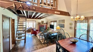 A spacious living area with a wooden staircase, a dining table with chairs, a fireplace, and a television. - August Place - Hot Tub, Community POOL, Game Table (Banner Elk)