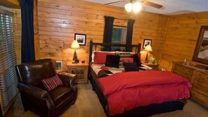 A wooden cabin bedroom with a bed, a leather chair, two bedside tables with lamps, and a ceiling fan. - August Place - Hot Tub, Community POOL, Game Table (Banner Elk)