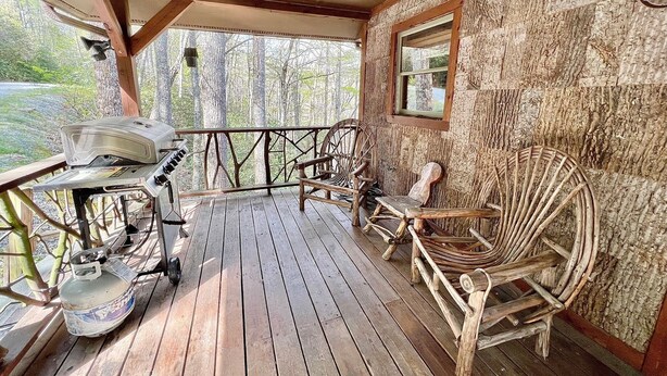 A wooden deck with a grill, wicker chairs, and a view of trees. - August Place - Hot Tub, Community POOL, Game Table (Banner Elk)