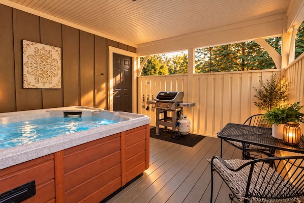 A hot tub on a wooden deck with a grill and seating area.