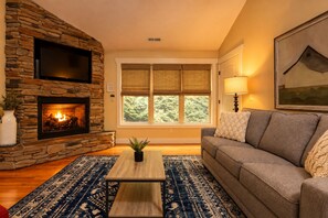 A living room with a stone fireplace, a sofa, a coffee table, and a large window with blinds.