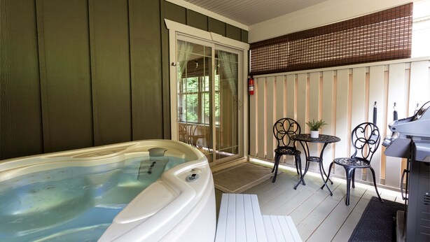 A hot tub on a porch with a covered seating area and a grill.