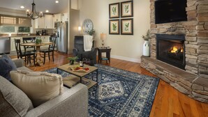A living room with a stone fireplace, a dining area with a chandelier, and a kitchen in the background.