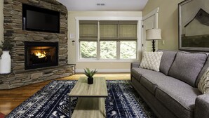 A living room with a stone fireplace, a flat-screen TV, a sofa, and a large window with blinds.