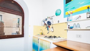 A small kitchen with a gas stove, a window, and a wooden table. - THE PANATICS Studio apartment (Gaeta, Italia)
