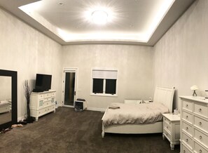 A bedroom with a bed, dresser, TV, and a ceiling light.