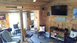 L’intérieur d’une cabane comprenant une télévision, un coin salon et un panneau indiquant qu’il s’agit d’une cabane à louer.