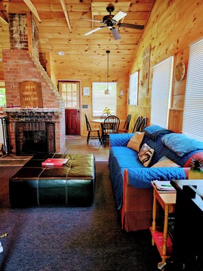 L’intérieur chaleureux d’un chalet comprend une cheminée, un coin repas et un espace salon confortable avec un canapé bleu et un pouf.