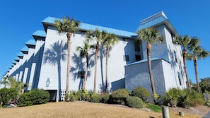 Stunning building with a unique architectural style, featuring a combination of white siding and blue roofing, surrounded by lush landscaping and palm trees.
