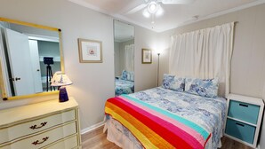 A bedroom with a bed, a dresser, a mirror, and a ceiling fan.