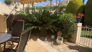 Un espace extérieur aménagé en patio, avec une table et des chaises, entouré de plantes en pot et d’une clôture décorative.