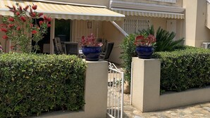 Un immeuble à plusieurs étages, doté d’une façade beige, de balcons blancs et d’un espace extérieur aménagé avec des plantes en pot.