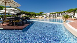 Un espace aménagé au bord de la piscine, avec des chaises longues et des parasols, une piscine carrelée et un bâtiment en arrière-plan.
