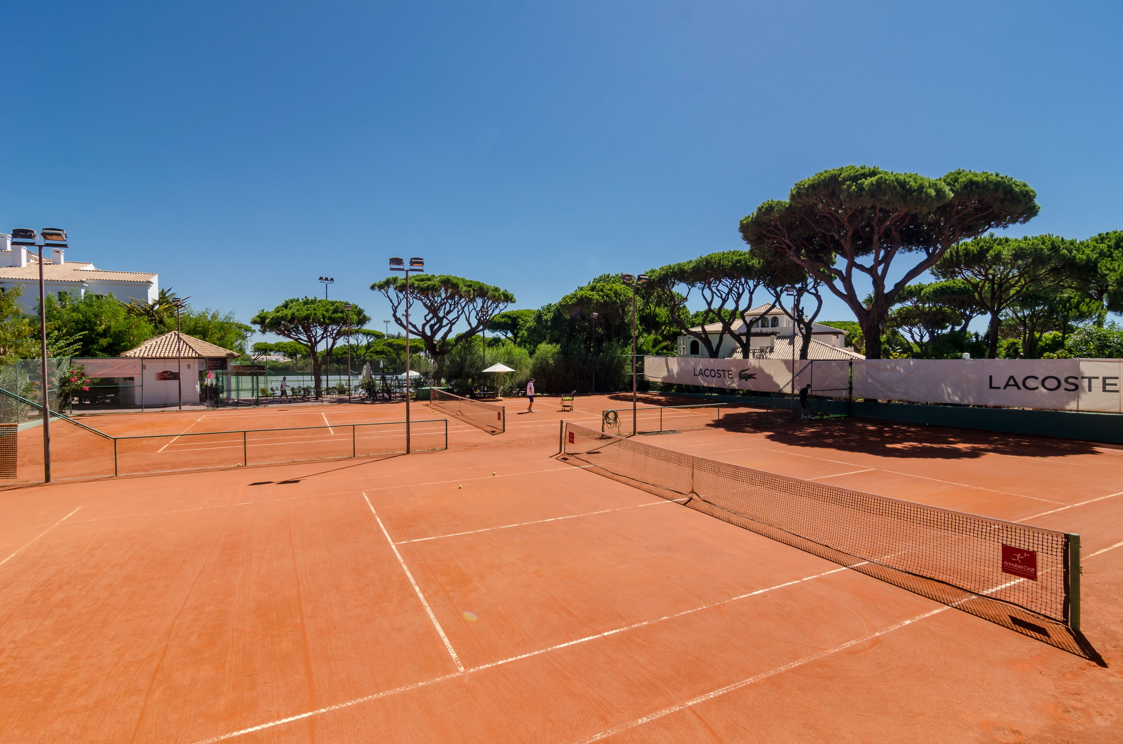 An outdoor tennis court with a net, surrounded by trees and buildings.