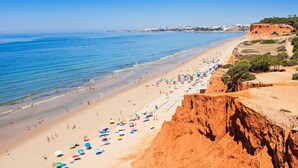 Une plage avec une longue étendue de sable, une falaise sur la droite et un ciel bleu dégagé.