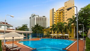 A swimming pool with lounge chairs and umbrellas, surrounded by palm trees and buildings. - Halong Pearl Hotel (Bai Chay)