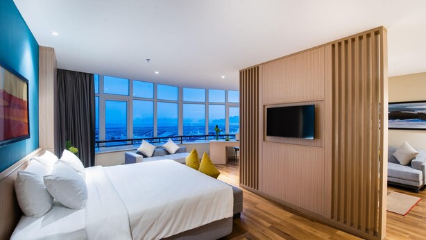 A modern hotel room with a large bed, a TV, and a balcony with a city view. - Halong Pearl Hotel (Bai Chay)