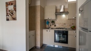 A modern kitchen with light-colored cabinets, a stainless steel oven, and a refrigerator. - Anchor Apartment (Marina di Ragusa)
