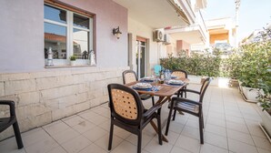 An outdoor dining area with a table set for four, surrounded by chairs, on a tiled patio adjacent to a building with a window and a door. - Anchor Apartment (Marina di Ragusa)