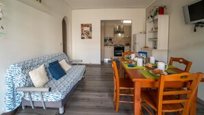 A modern living room with a sofa, dining table, chairs, and a kitchen in the background. - Anchor Apartment (Marina di Ragusa)