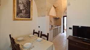 Uma sala de jantar com uma mesa posta para quatro pessoas, um quadro na parede e uma TV sobre um suporte de madeira.