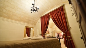 Quarto com uma cama grande, cortinas vermelhas, um candelabro e um espelho com moldura dourada.