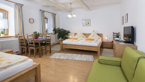 Una habitación acogedora con cama, sofá verde, mesa de madera con sillas, escritorio pequeño y televisor.