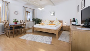 Un dormitorio con una cama de madera, un escritorio, una silla, una planta en maceta, un reloj y un televisor.