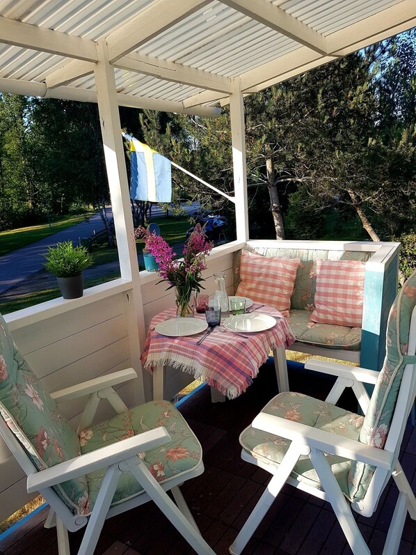 A covered outdoor seating area with a table set for two, surrounded by floral-patterned chairs.