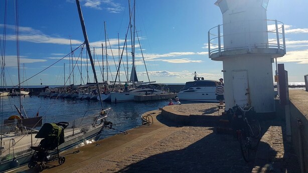 A harbor with boats docked, a lighthouse, and a clear sky.